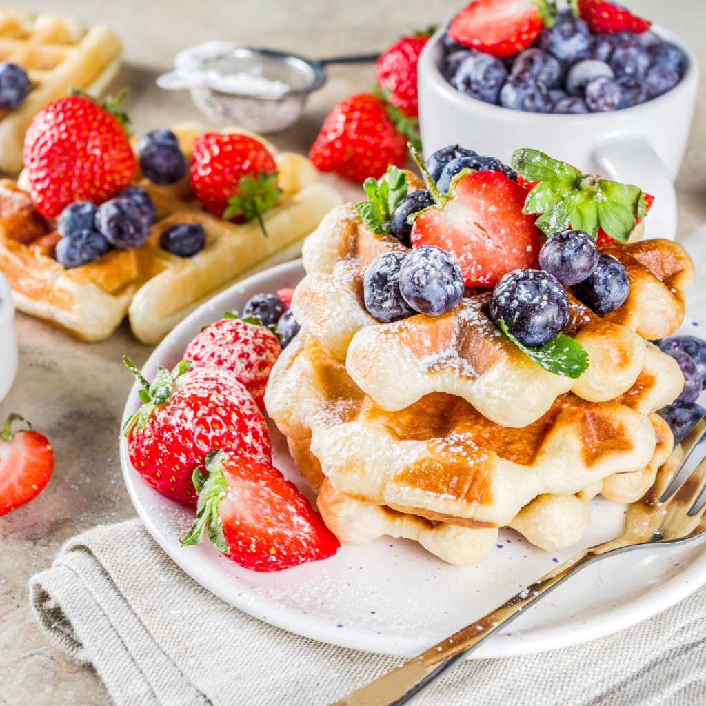 Вкусные сладкие вафли с ягодами клубники, черники и сахарной пудрой