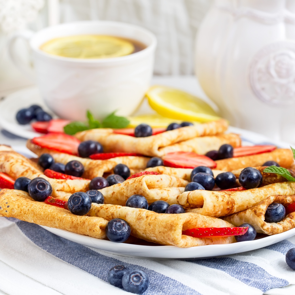 Тонкие блинчики с ягодами черники и клубники на столе с чаем