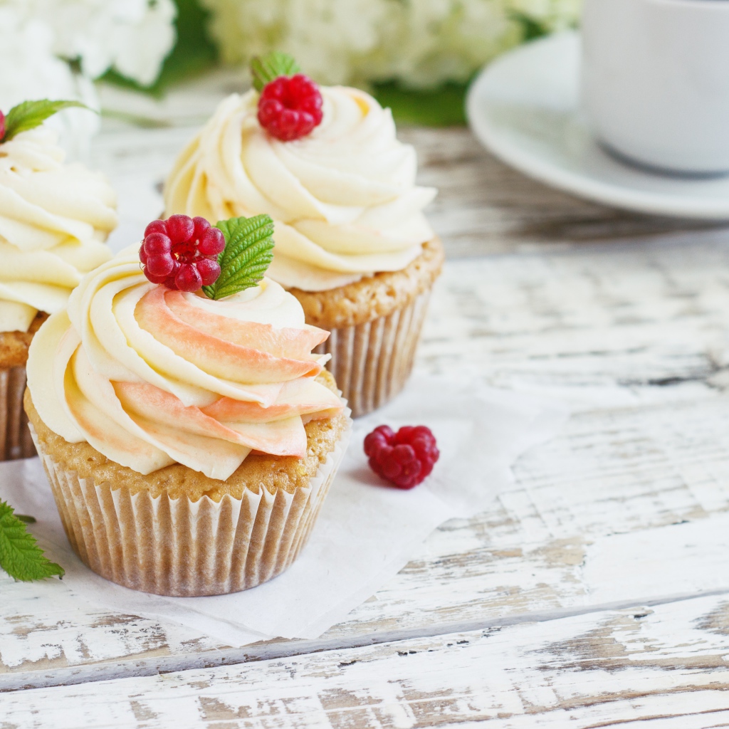 Три кекса с кремом на столе с чашкой кофе