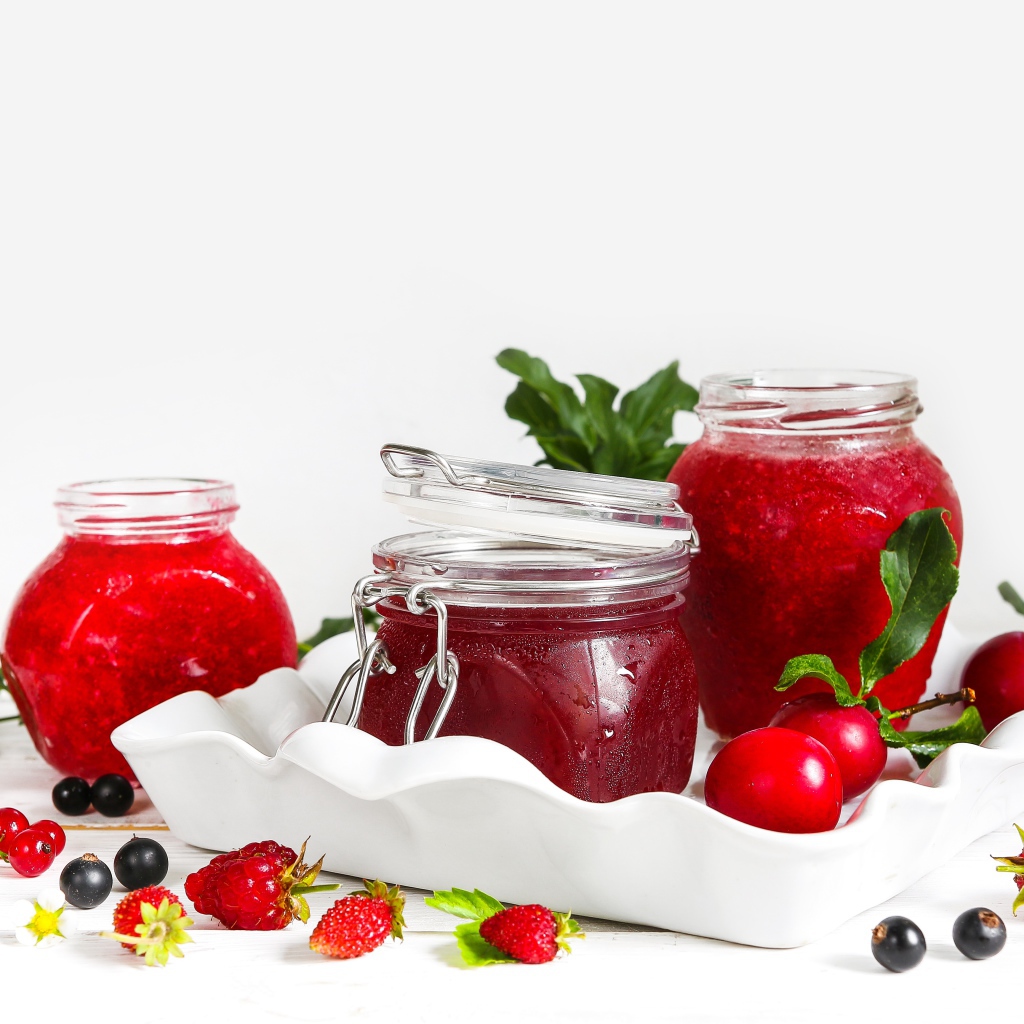 Три банки джема с ягодами на белом фоне