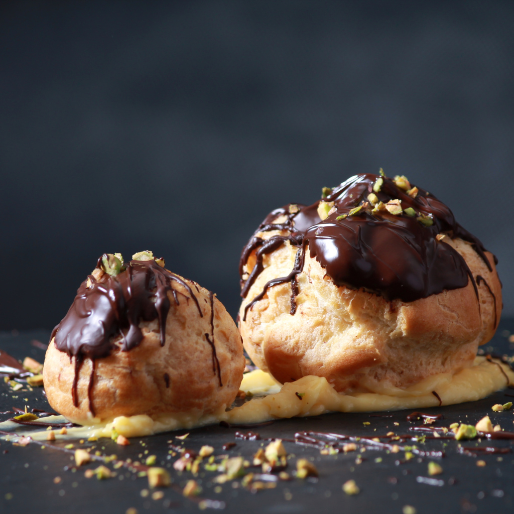 Два заварных пирожных с шоколадом на сером фоне