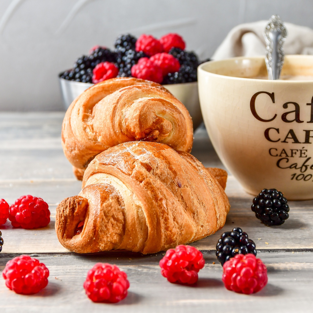 Два круассана с малиной, черникой и чашкой кофе на столе