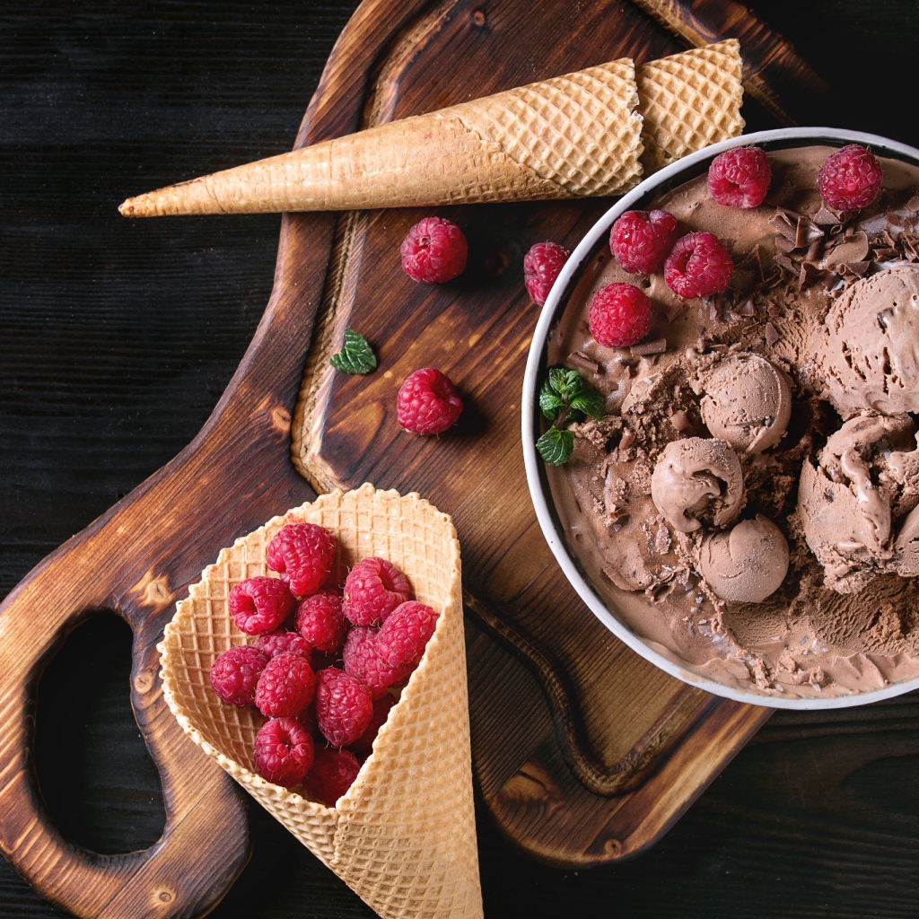 Вафельный рожок с шоколадным мороженым и ягодами малины на столе