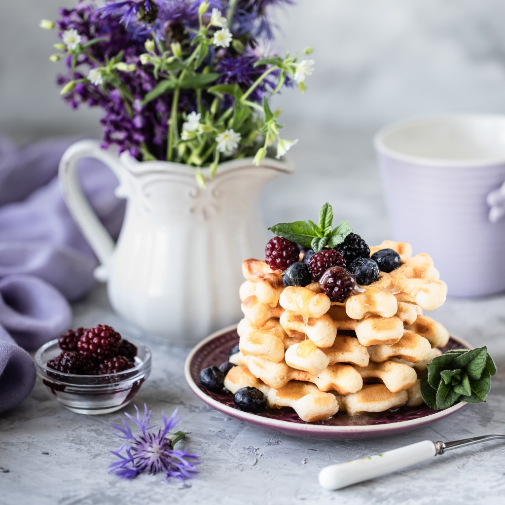 Вафли с ягодами черники и ежевики на столе с букетом