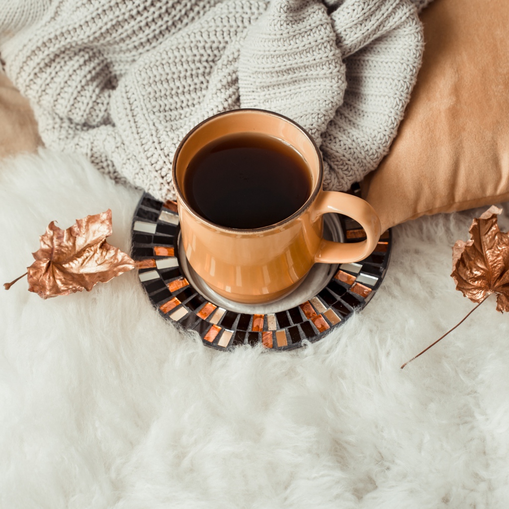 Чашка кофе стоит на покрывале с теплым свитером 