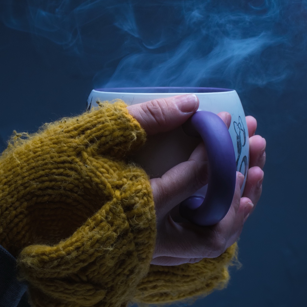 Чашка горячего кофе в руках у девушки на сером фоне