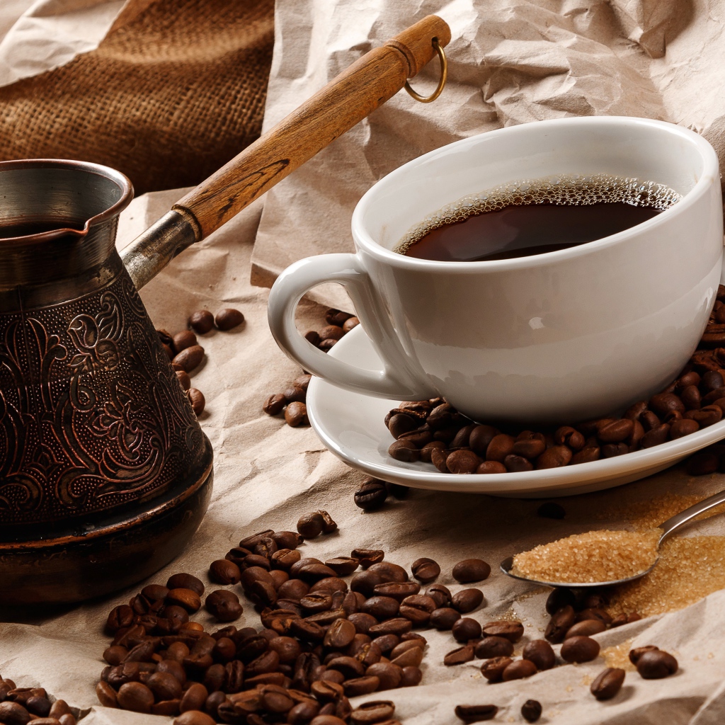 Чашка горячего кофе на столе с туркой, зернами и коричневым сахаром