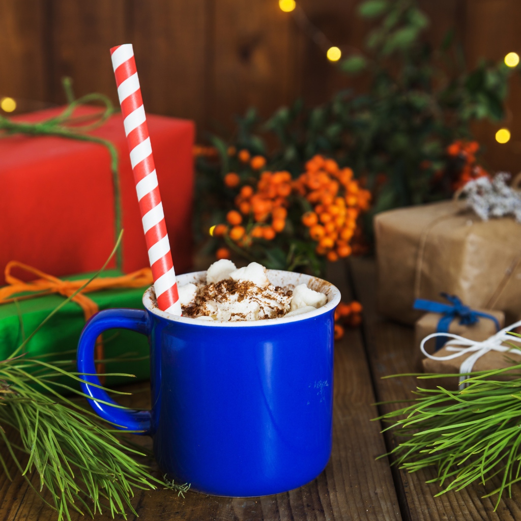 Синяя чашка горячего шоколада с маршмеллоу на столе с еловыми ветками и подарками