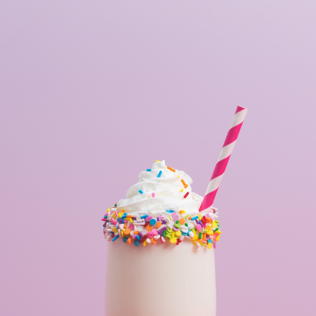 Коктейль  в стакане со взбитыми сливками на розовом фоне