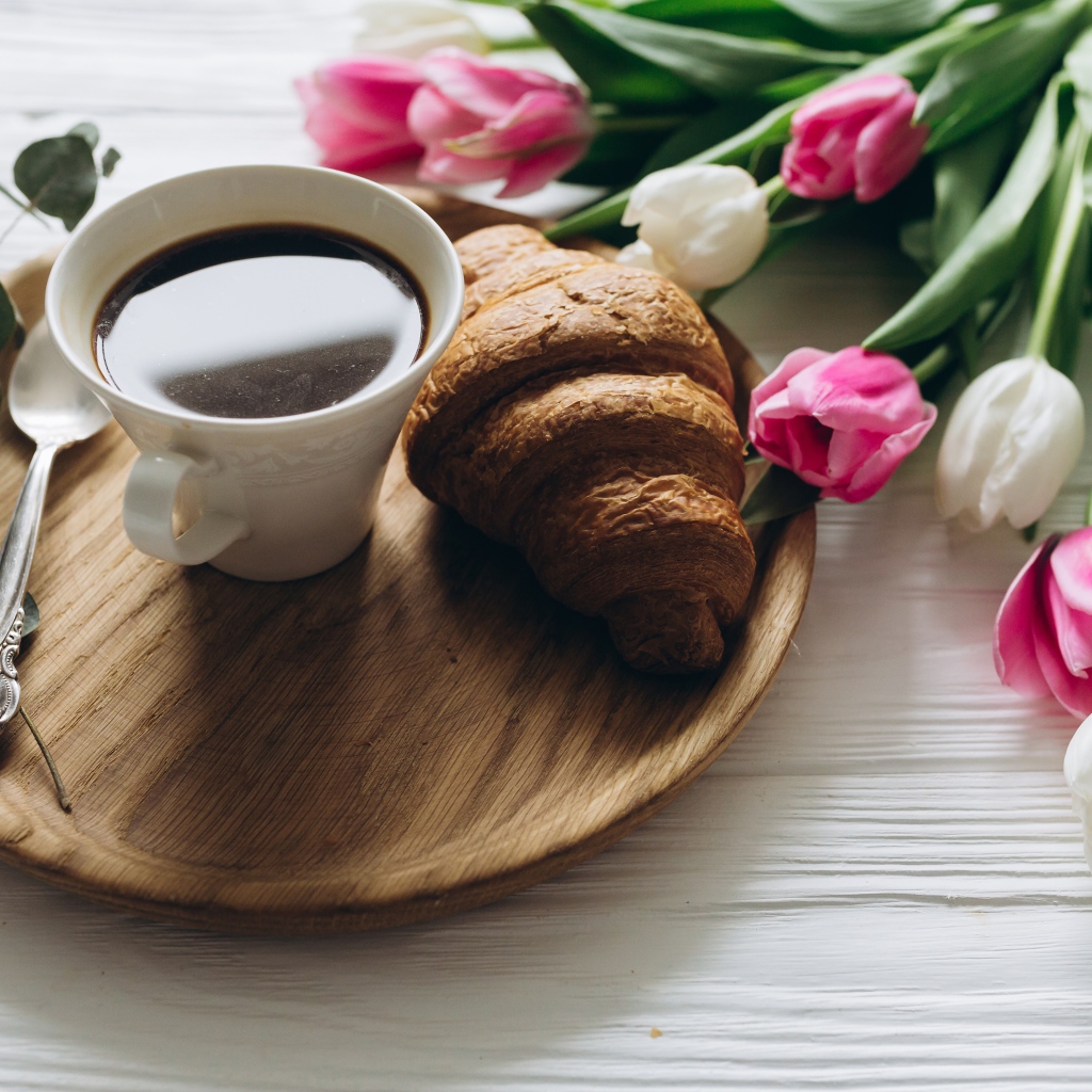 Чашка кофе и круассан на столе с букетом тюльпанов