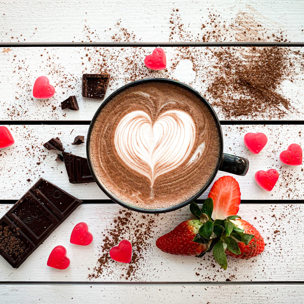 Чашка кофе с рисунком на пене на столе с шоколадом и клубникой 