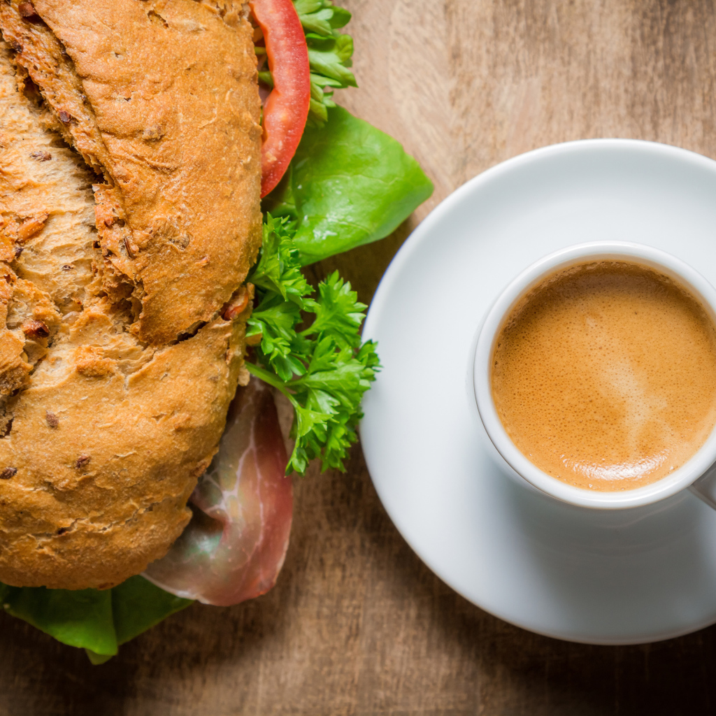 Чашка кофе с бутербродом на столе к завтраку 