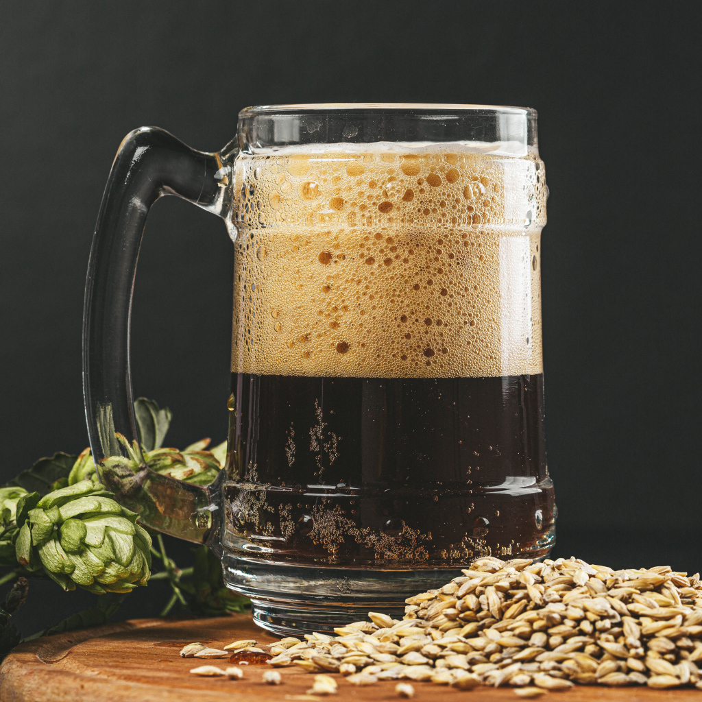 Темное пиво в бокале на столе с хмелем и зернами пшеницы 