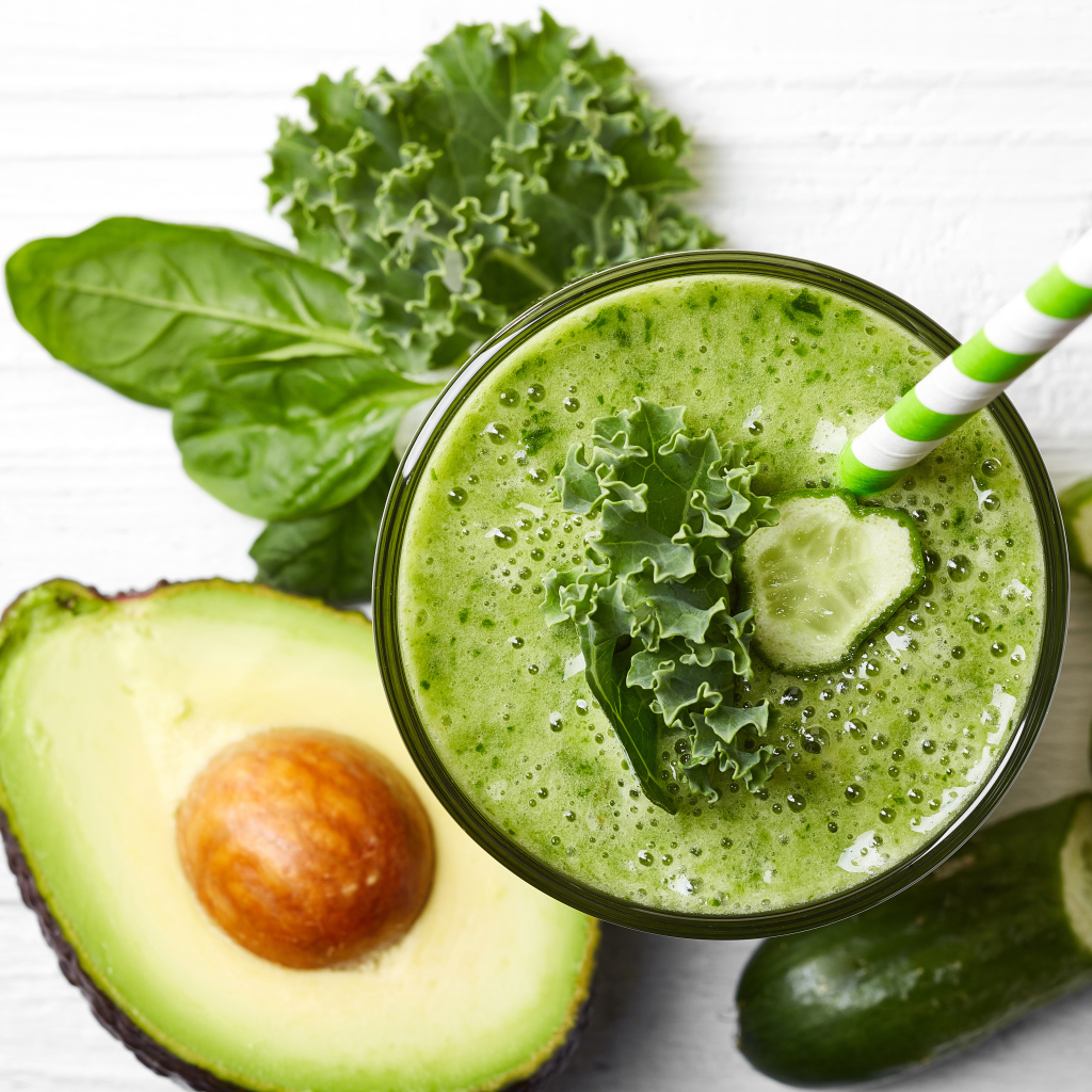 Зеленый смузи на столе с огурцом, авокадо и зеленью