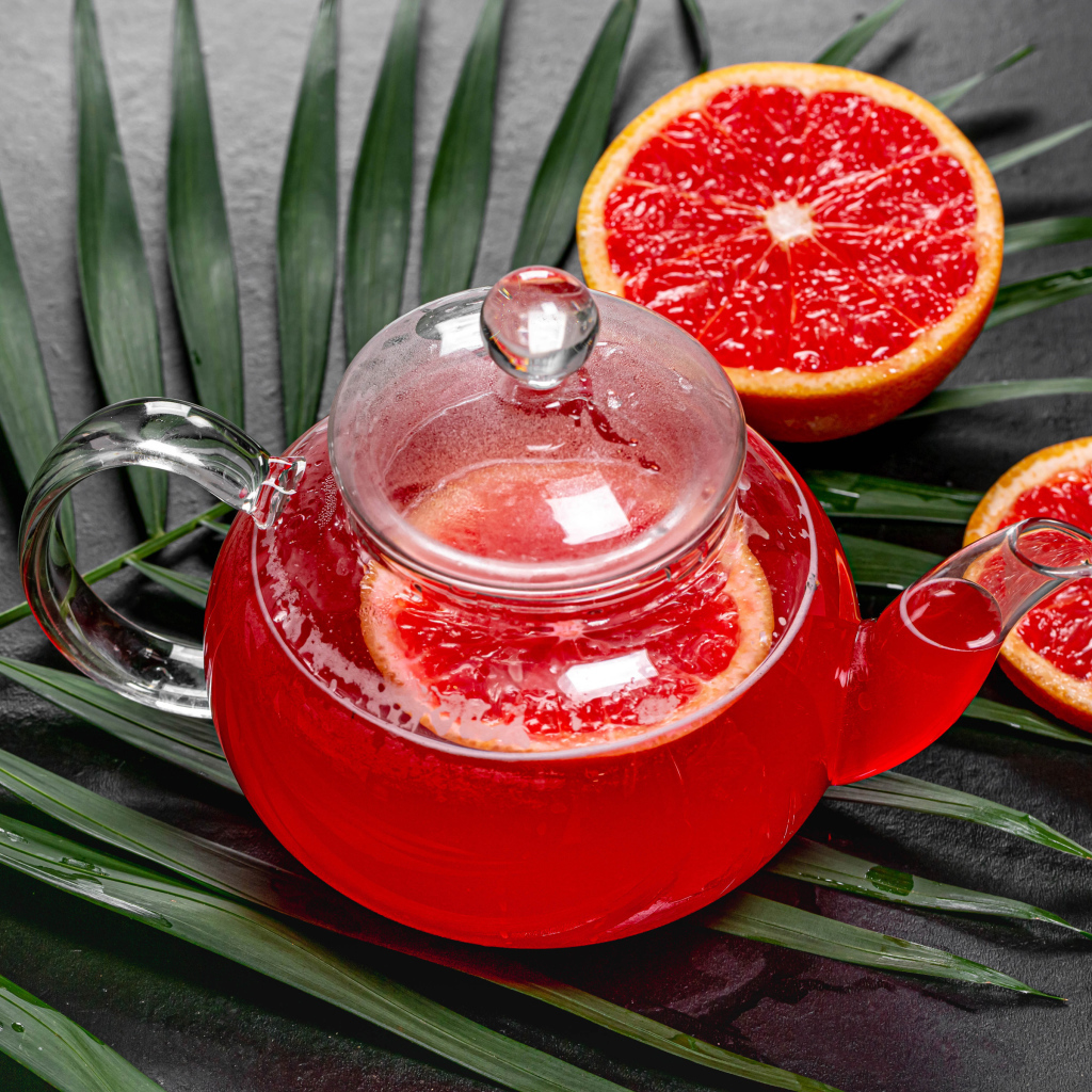 Красный чай в чайнике на столе в грейпфрутом и листьями