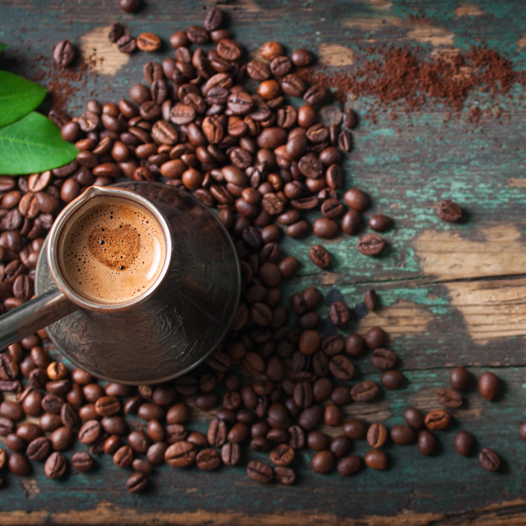 Турка с кофе на столе с зернами и зелеными листьями