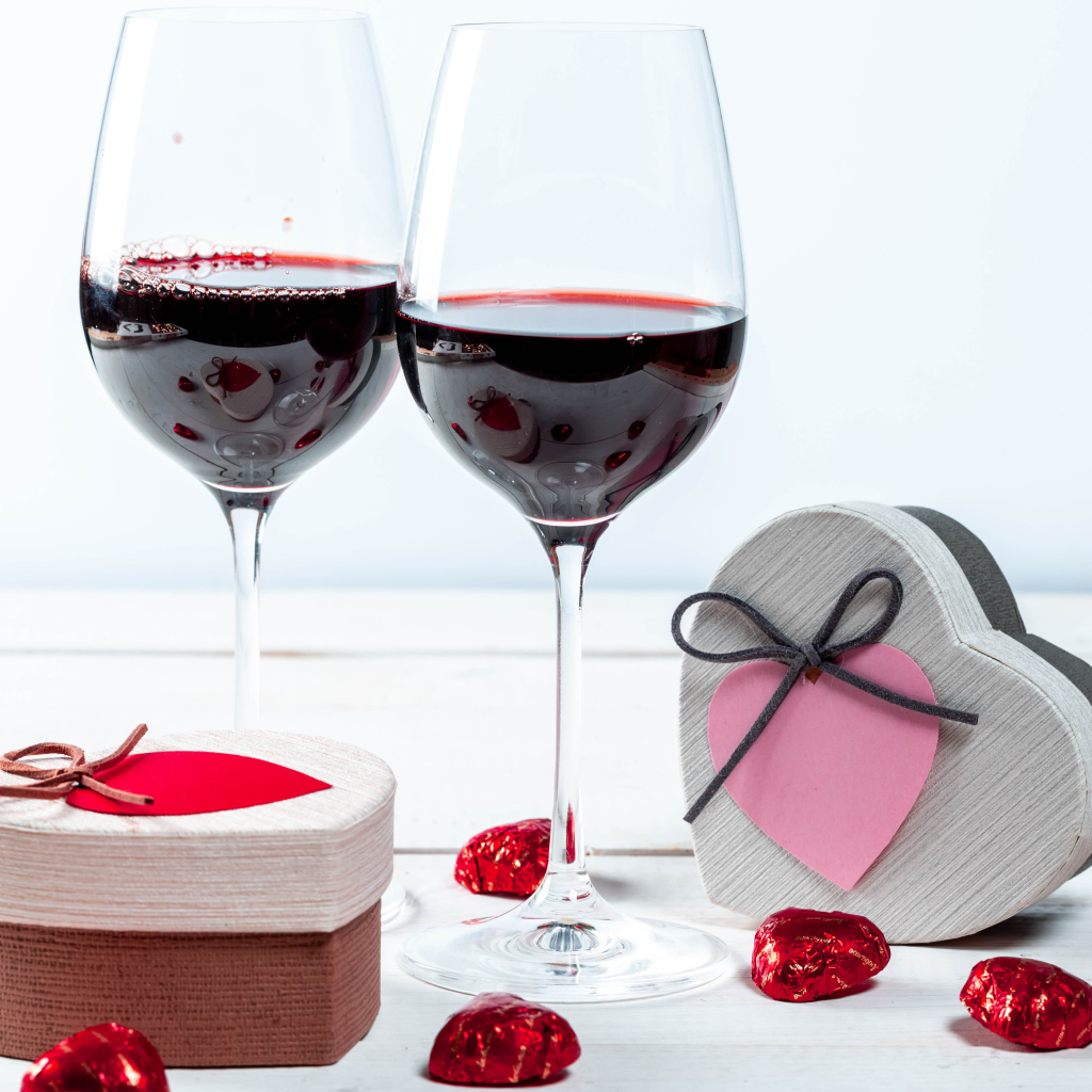 Две коробки с конфетами в форме сердца на столе с бокалами 