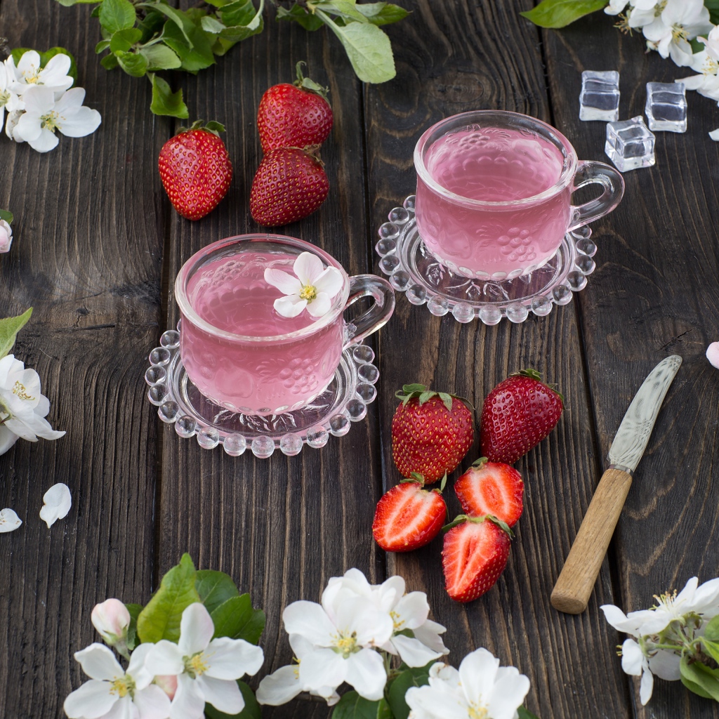 Две стеклянные чашки ягодного чая на столе с клубникой и цветами яблони