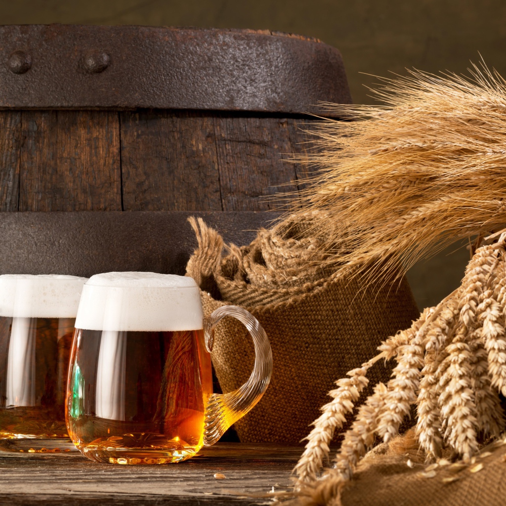 Два бокала пива на столе с колосьями пшеницы  и бочкой