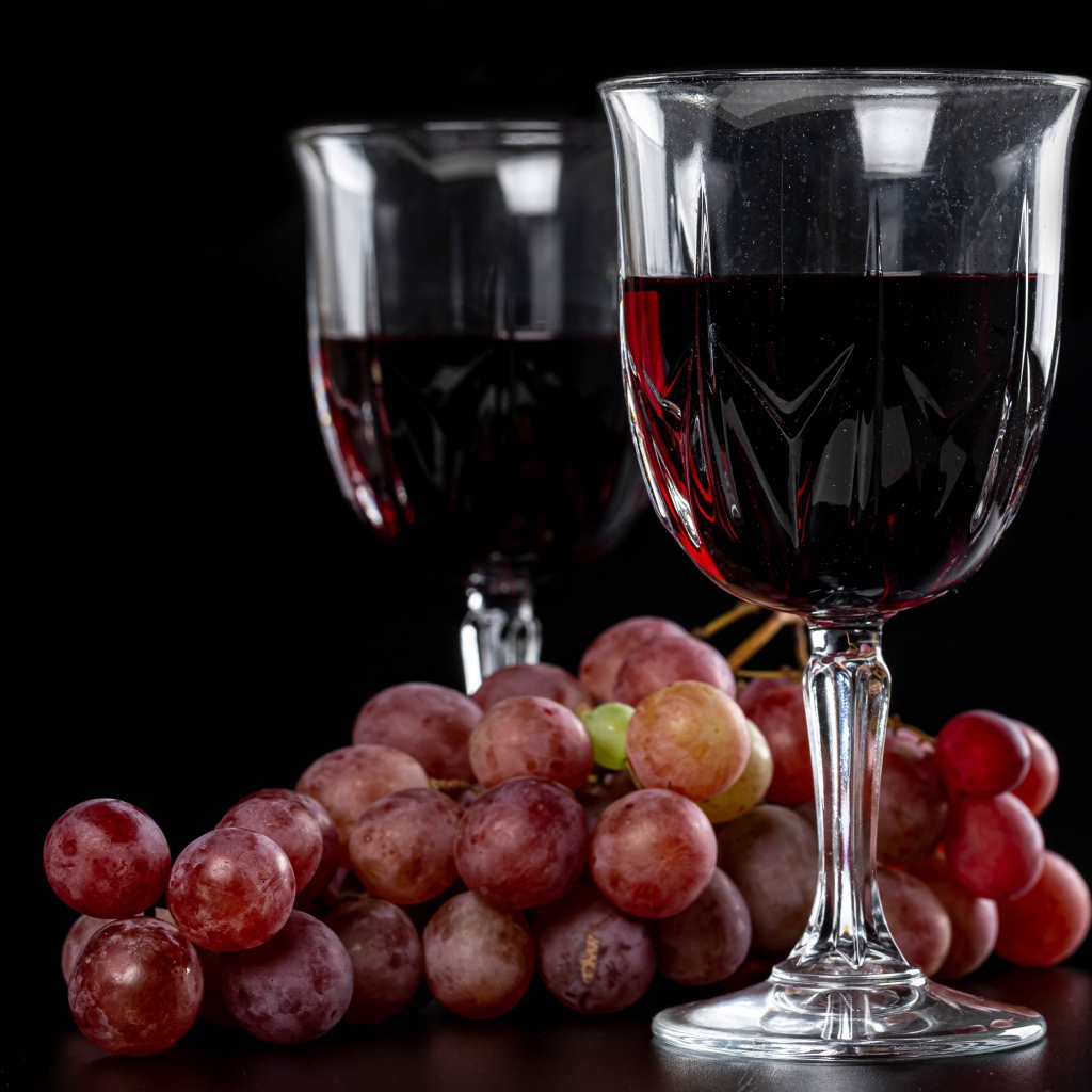 Два бокала вина на черном фоне с виноградом 