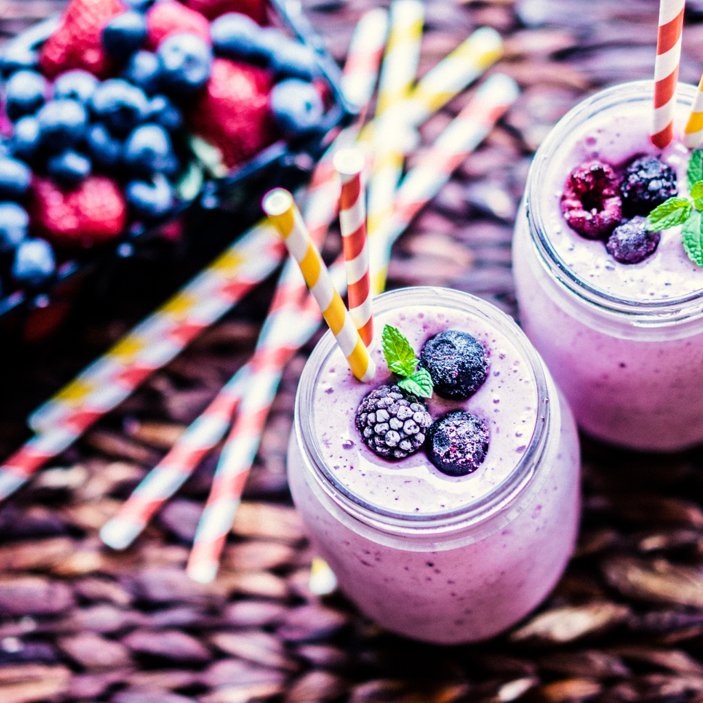 Две банки смузи с трубочками на столе с ягодами