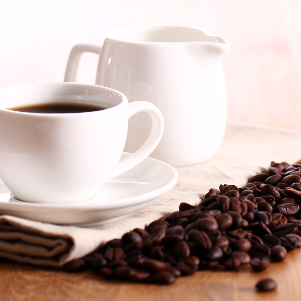 Белая чашка кофе на столе с молоком и зернами