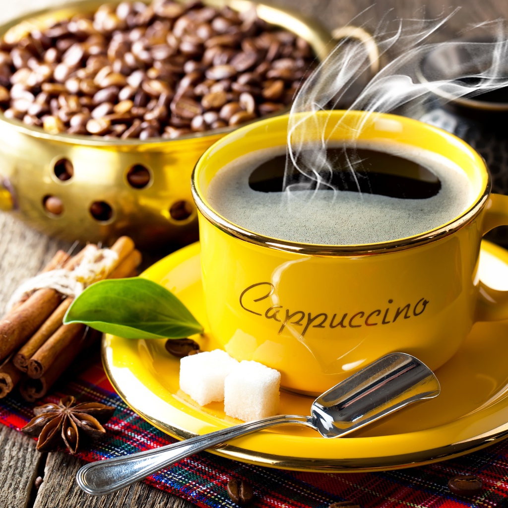 Желтая чашка с горячим кофе на столе с зернами и корицей 