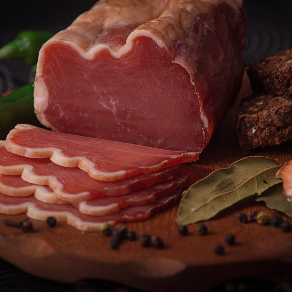 Кусок вяленого мяса на доске с черным хлебом и специями