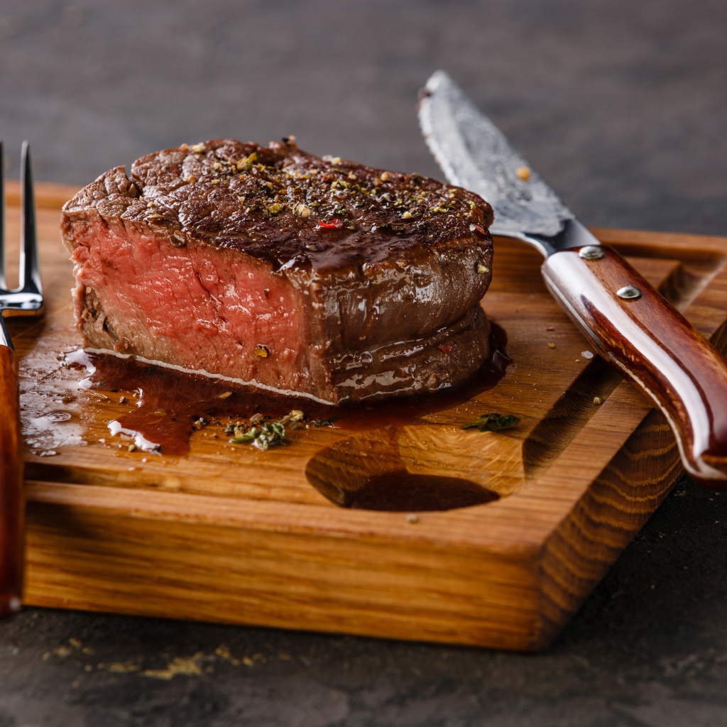 Кусок сочного мяса на доске с ножом и вилкой 