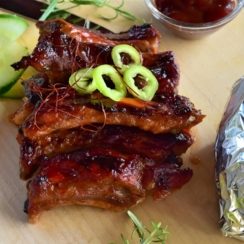 Аппетитные жареные ребрышки на столе с огурцами  и соусом 