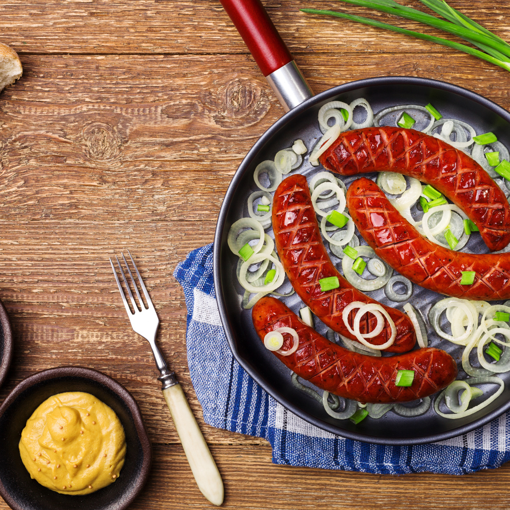 Колбаски барбекю с луком на сковороде на столе с соусом