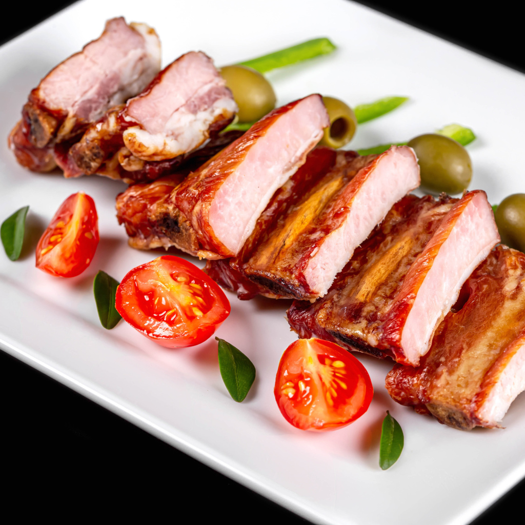 Запеченные ребрышки на белой тарелке с помидорами и оливками