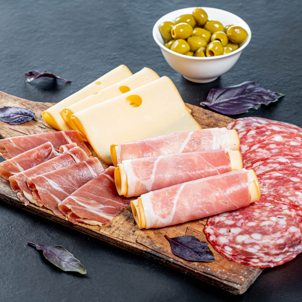 Сыр, бекон и колбаса на разделочной доске на столе с оливками