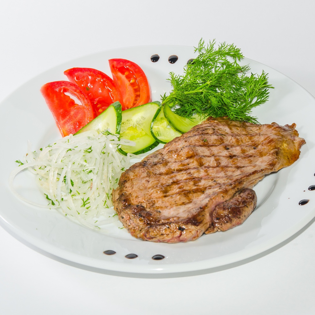 Кусок курицы с овощами на белой тарелке 