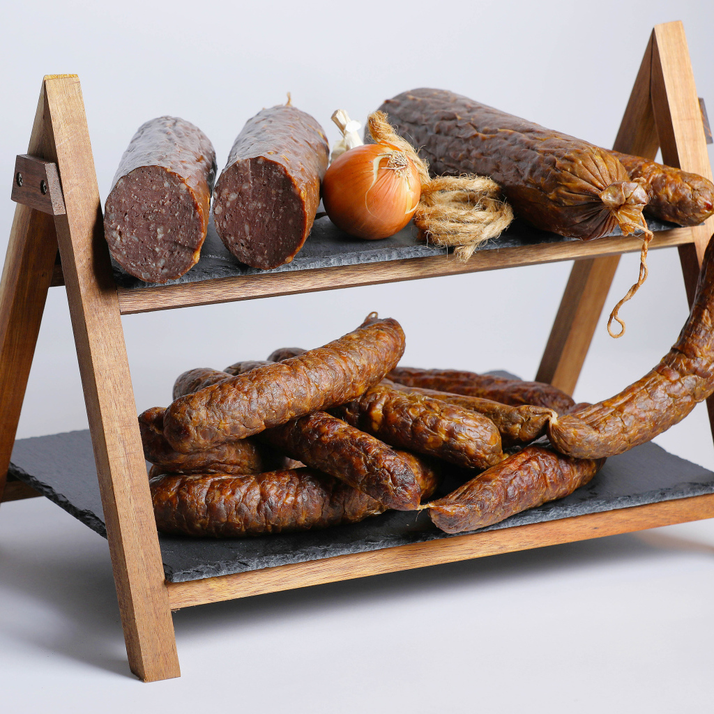 Различные виды колбасы на полке с луком на сером фоне