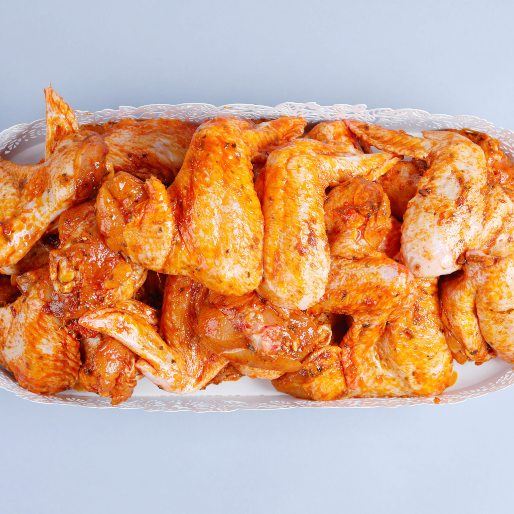 Жареные куриные крылья в белой корзине на сером фоне