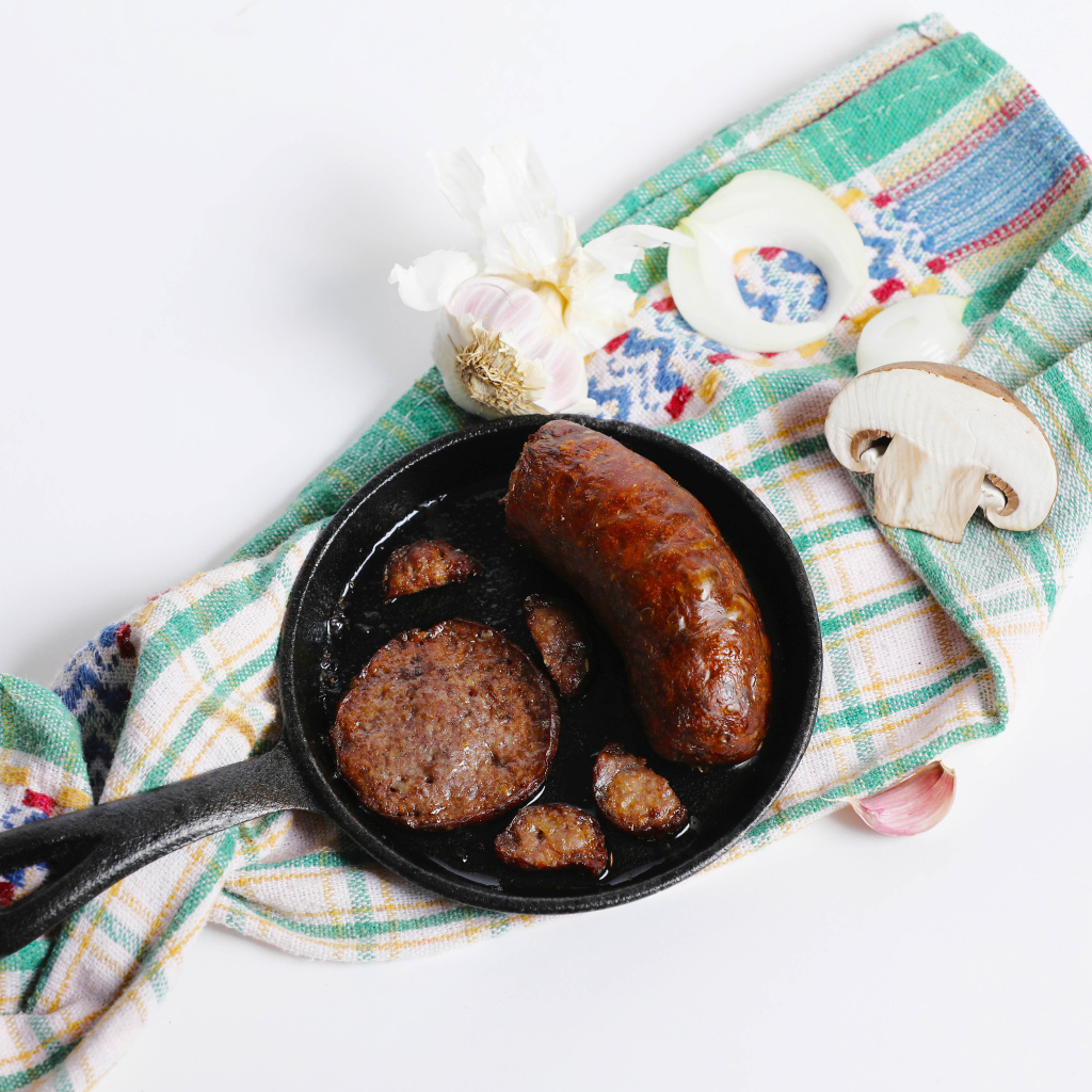 Сковорода с жареной колбасой на столе с полотенцем и чесноком