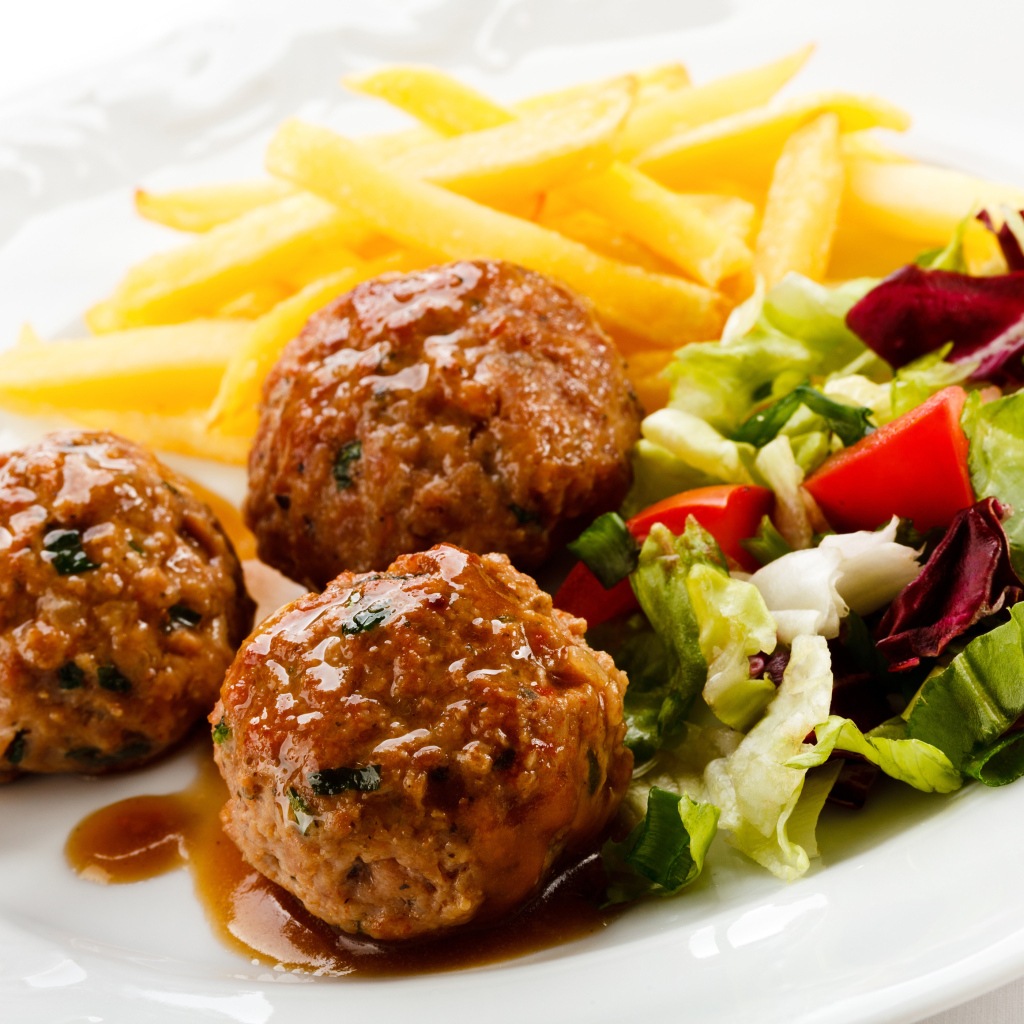 Фрикадельки с салатом и картофелем фри на белой тарелке