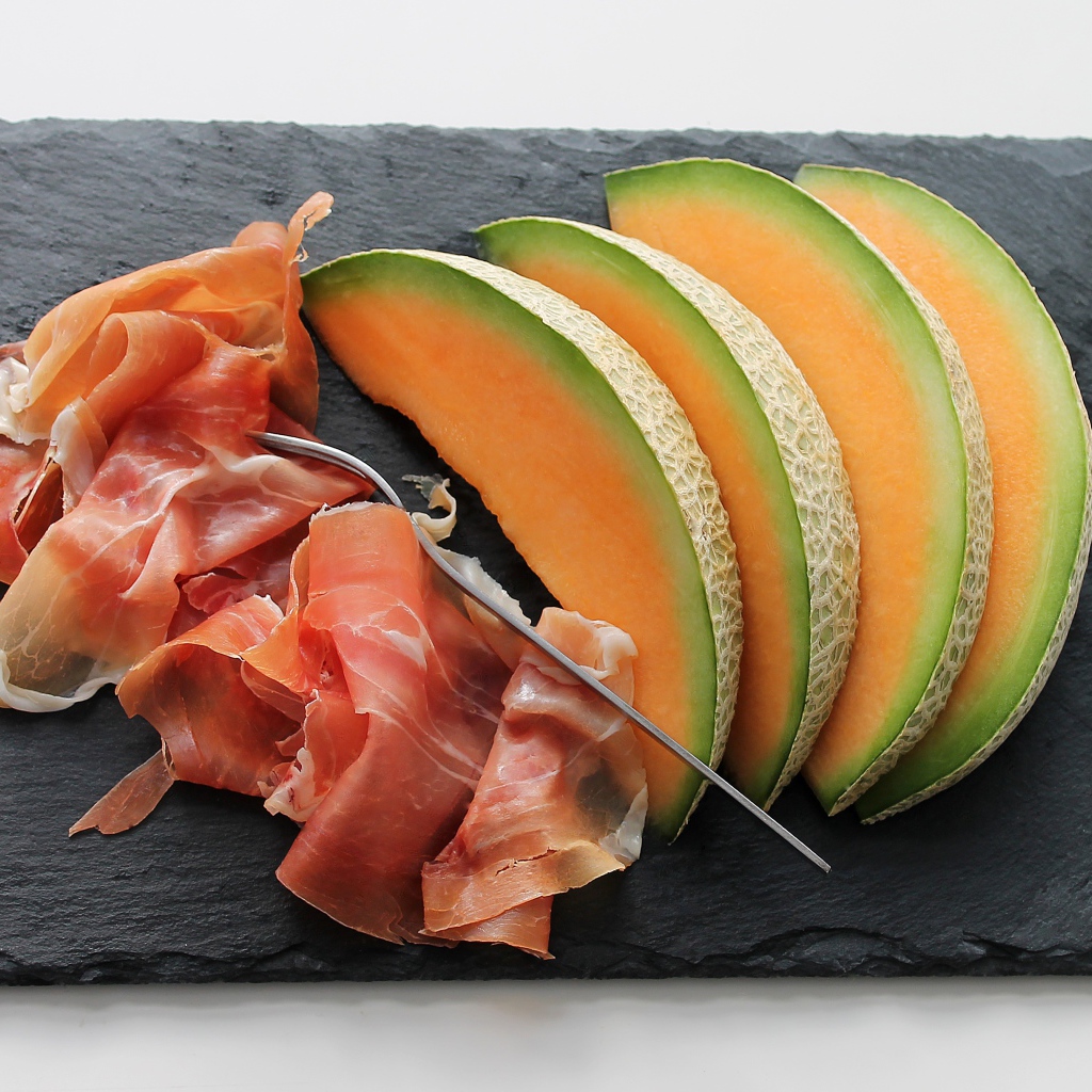 Кусочки дыни на доске с прошутто