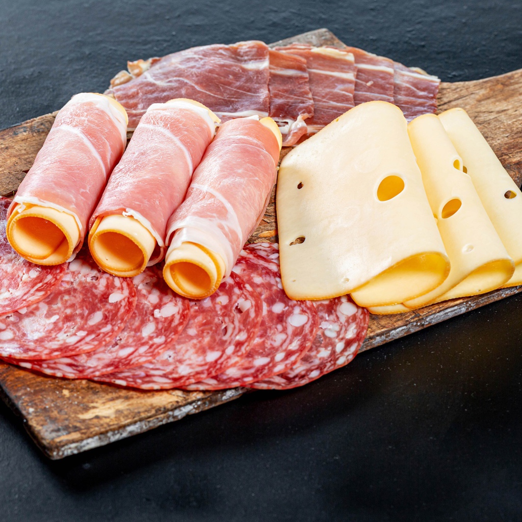 Куски сыра, ветчины и колбасы на доске