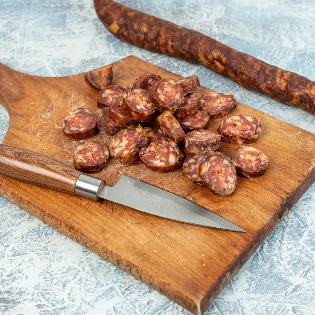 Колбаса нарезана колечками на разделочной доске с ножом 