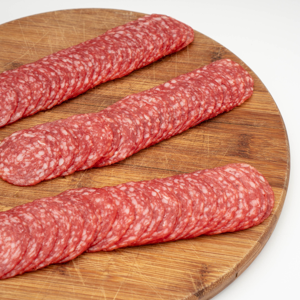 Колбаса тонко нарезана на разделочной доске 