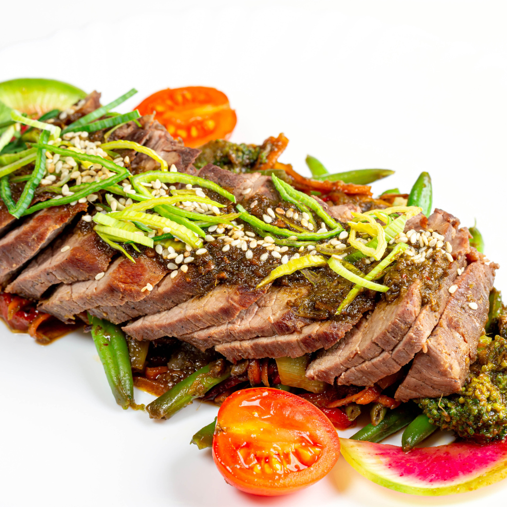 Мясо нарезанное кусочками на белом фоне с овощами