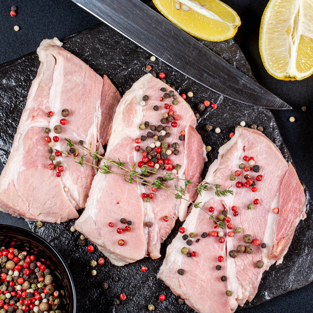 Куски свежего мяса на столе с зернами перца и лимоном