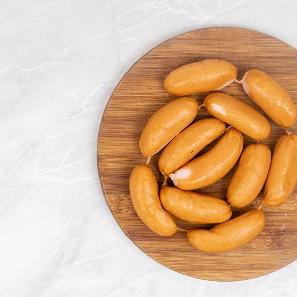 Копченые сардельки на деревянной доске на сером фоне