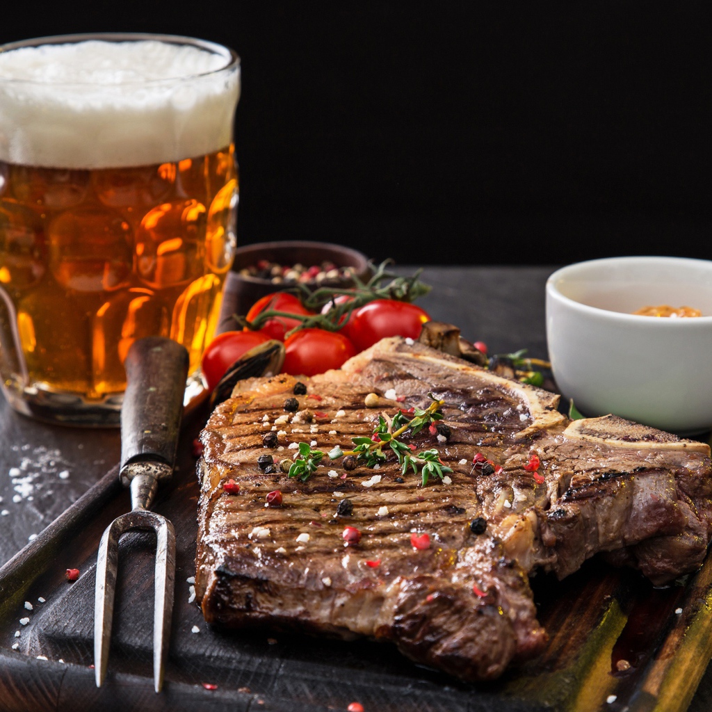 Вкусный кусок мяса на столе с помидорами и бокалом пива