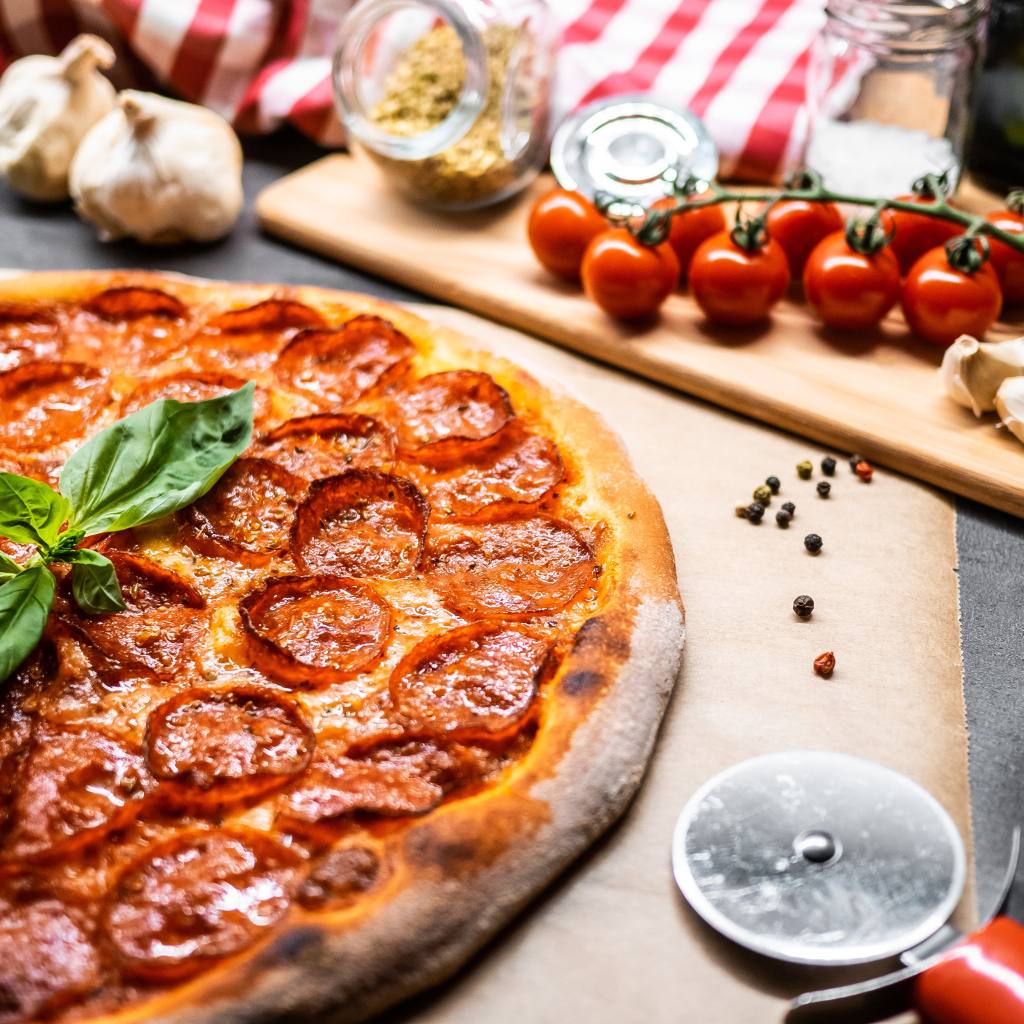 Пицца пепперони на столе с овощами и специями