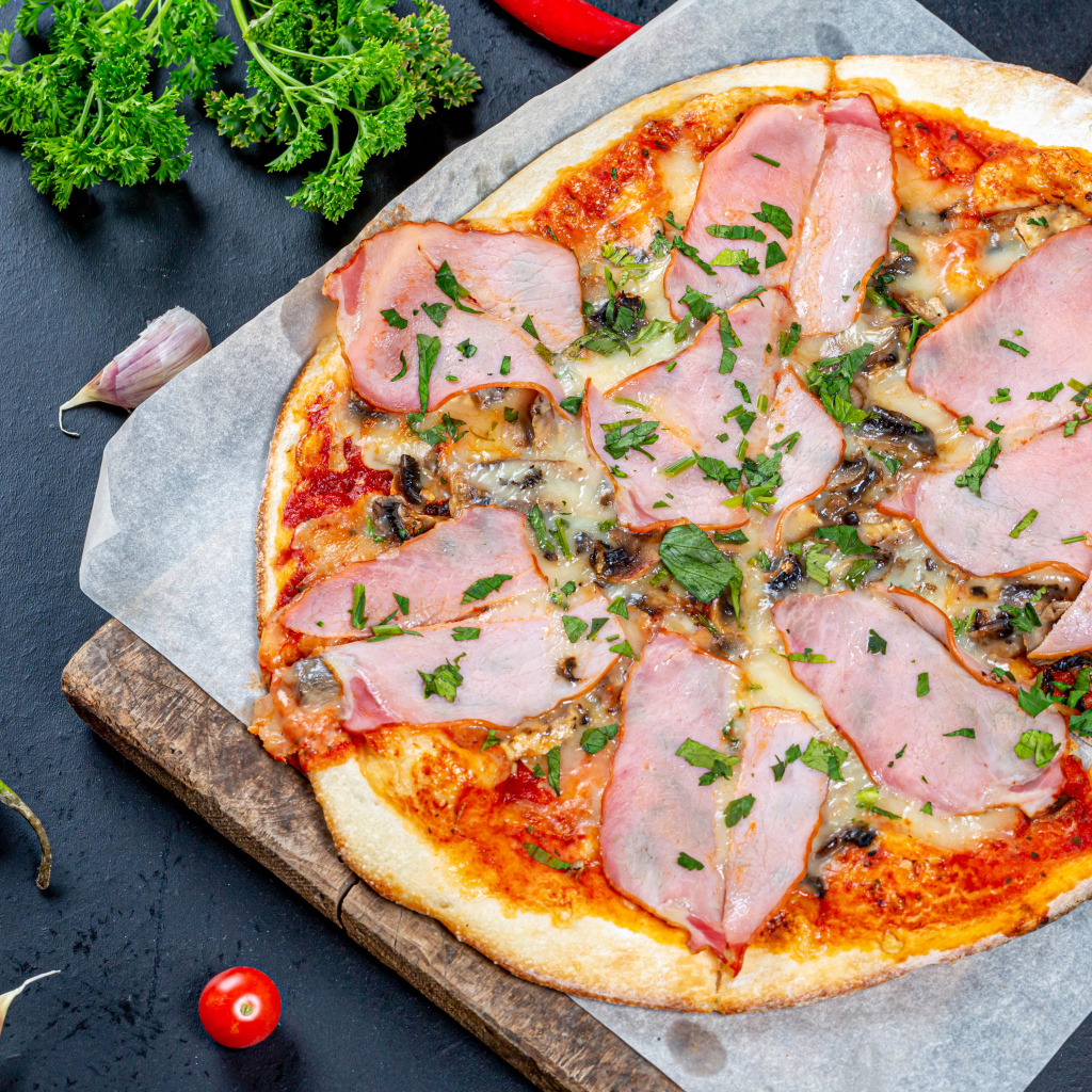 Пицца с ветчиной и грибами на столе с перцем чили, чесноком и петрушкой