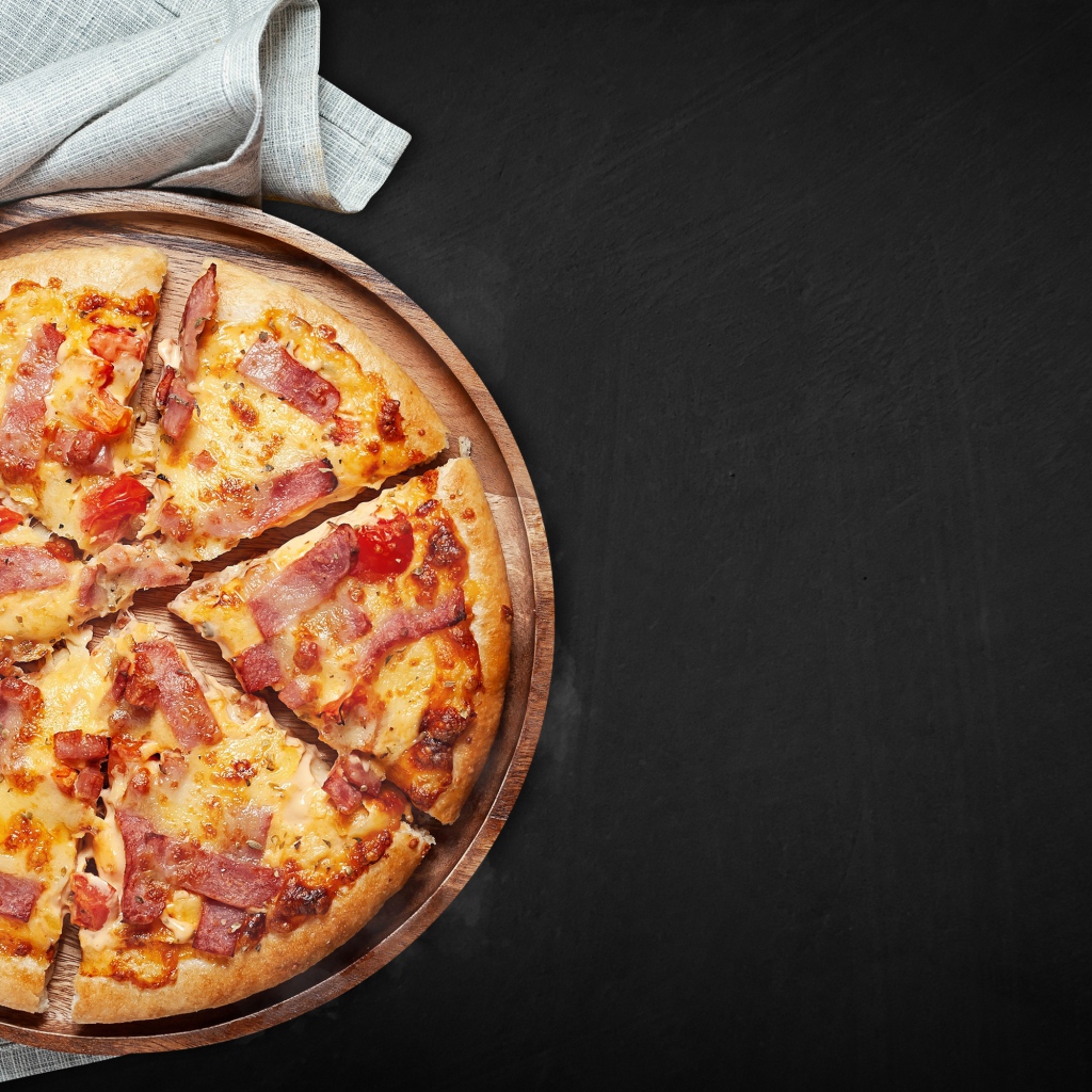 Пицца с кусочками бекона на доске на черном фоне