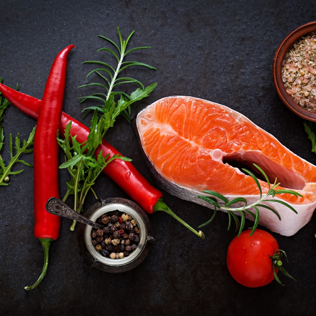 Кусок свежей красной рыбы на столе со специями, красным перцем и помидорами